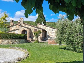 Ein Steinhaus mit Garten und einer hügeligen Landschaft im Hintergrund.