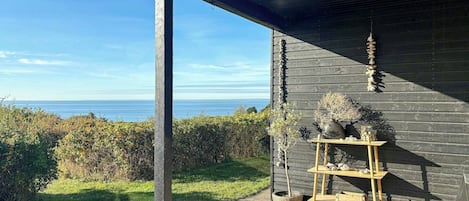 A modern building with a dark exterior, a wooden shelf with decorative items, and a view of the sea.