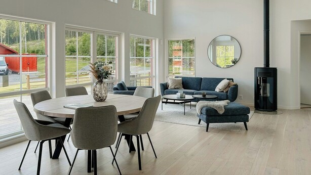Una amplia sala de estar con techos altos, ventanas grandes, chimenea y un comedor con sillas y mesa.