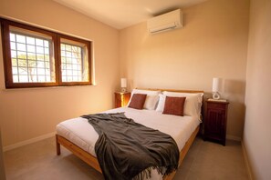Ein Schlafzimmer mit einem Bett, Nachttischen, einer Klimaanlage und einem Fenster mit Jalousien.