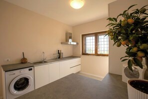 Eine kleine Küche mit Waschmaschine, Spüle und einem Fenster mit Jalousien.