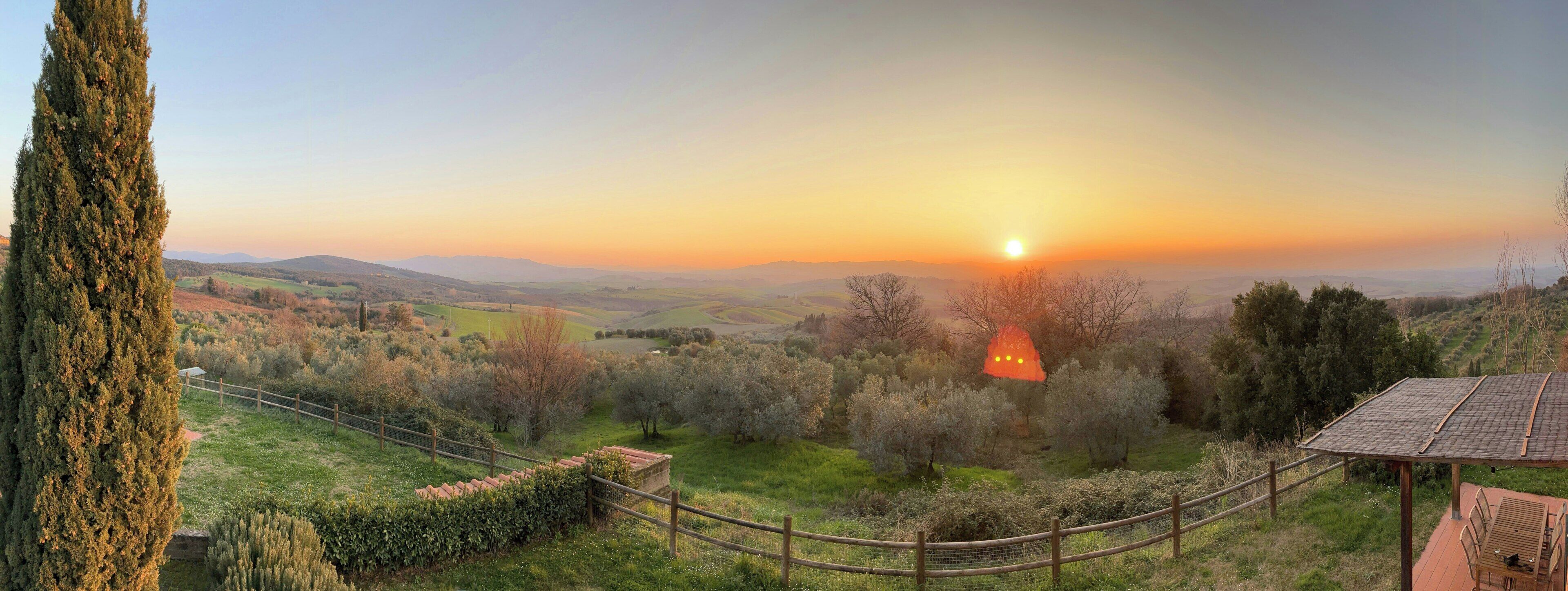 A scenic view of a countryside landscape with a sunset, a tall tree, and a wooden fence.