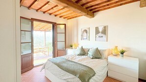 A bedroom with a bed, a nightstand, a chair, a window, and a door leading to an outdoor area. - Tuscan apartment with panoramic views in Iano (Montaione FI)