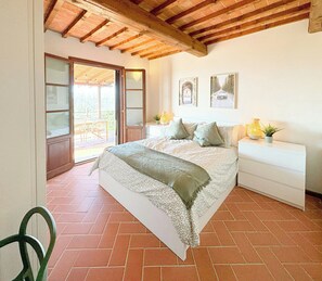 A bedroom with a bed, a nightstand, a chair, a window, and a door leading to an outdoor area. - Tuscan apartment with panoramic views in Iano (Montaione FI)