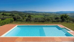 A rectangular swimming pool with a clear blue water surface, surrounded by a brick patio. - Tuscan apartment with panoramic views in Iano (Montaione FI)