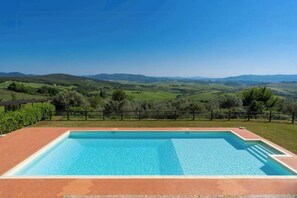 A rectangular swimming pool with a clear blue water surface, surrounded by a brick patio. - Tuscan apartment with panoramic views in Iano (Montaione FI)