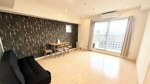 A spacious living area with a black sofa, a dining table with chairs, a black wall with a unique pattern, and a large window with a view of buildings. - Olfea Namba South No.11 (Osaka)