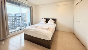 A modern bedroom with a bed, a window with curtains, an air conditioning unit, and a view of buildings outside. - Olfea Namba South No.11 (Osaka)