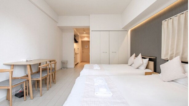A modern hotel room with a long bed, a desk with chairs, and a wardrobe. - Olfea Namba South No.11 (Osaka)