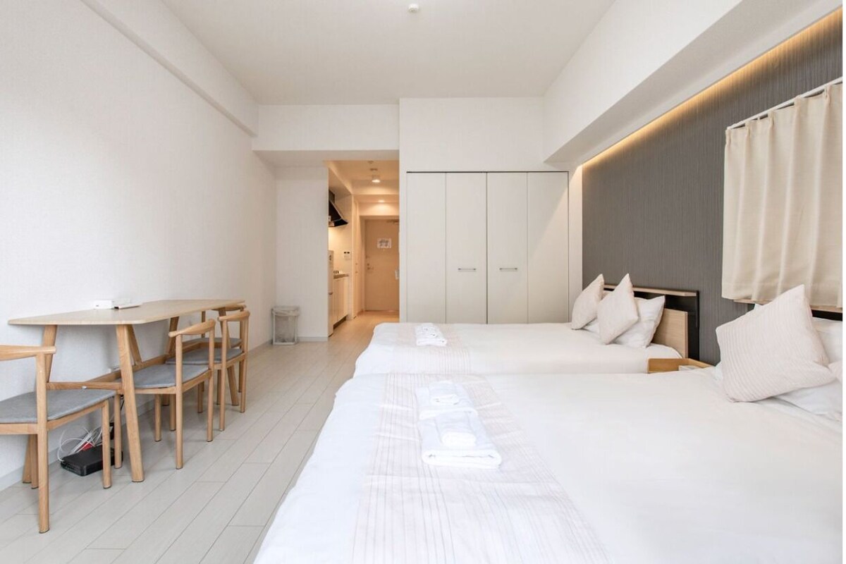A modern hotel room with a long bed, a desk with chairs, and a wardrobe.
