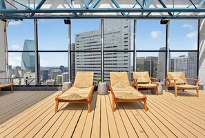 Eine Dachterrasse mit Holzboden, Liegestühlen und Blick auf die Stadt.