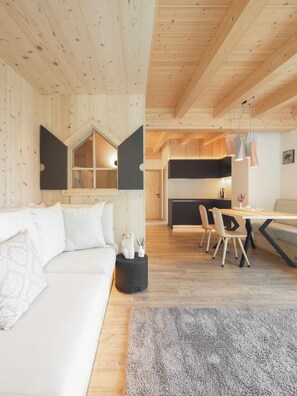 A modern interior with a wooden ceiling, a white sofa, a dining area with chairs, and a kitchen in the background.