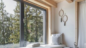 A room with a built-in bench, large windows, a wooden ceiling, and a view of trees. - Alpine flats in Fai della Paganella (Fai della Paganella)