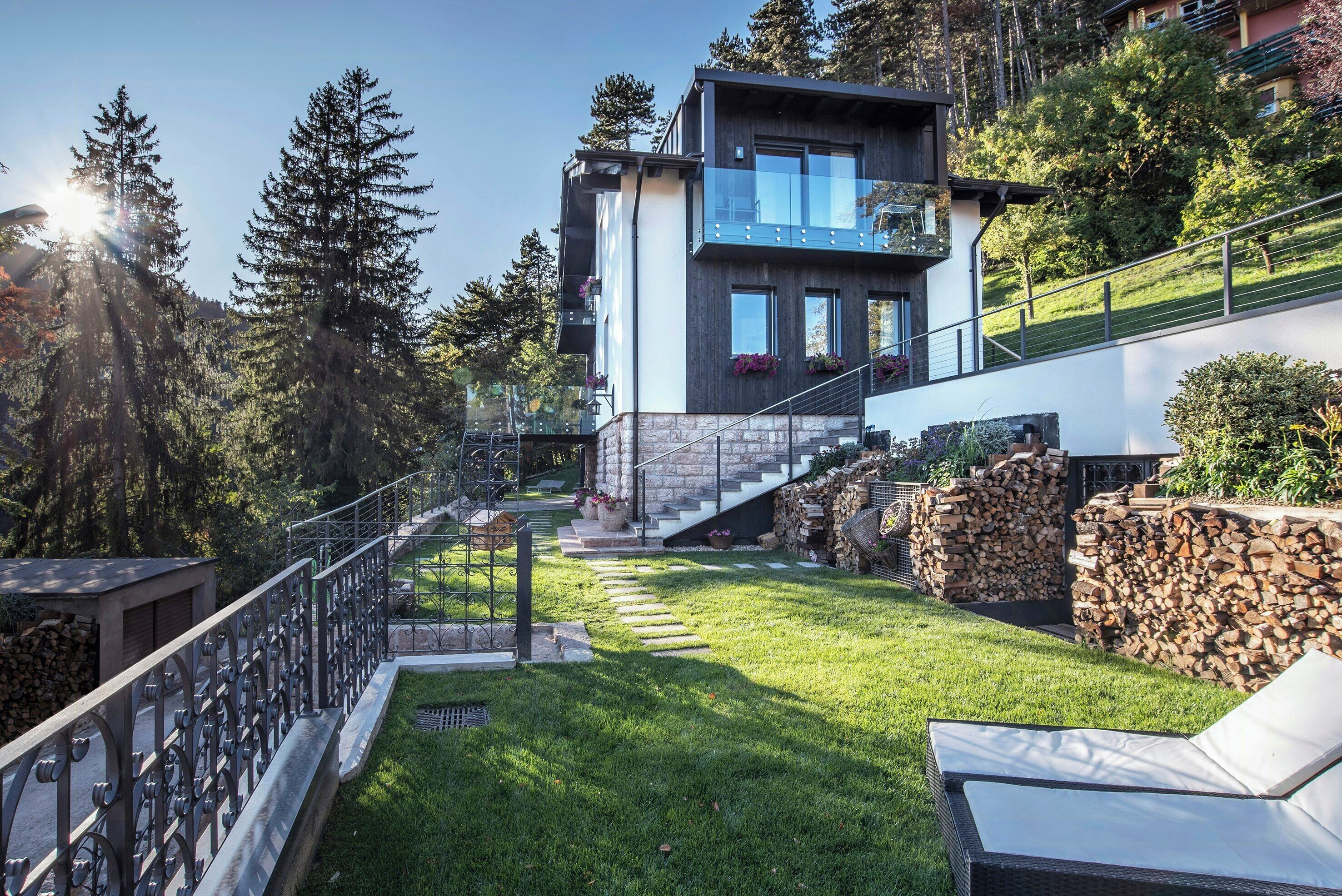 A modern house with a glass balcony, a stone staircase, and a well-maintained lawn.