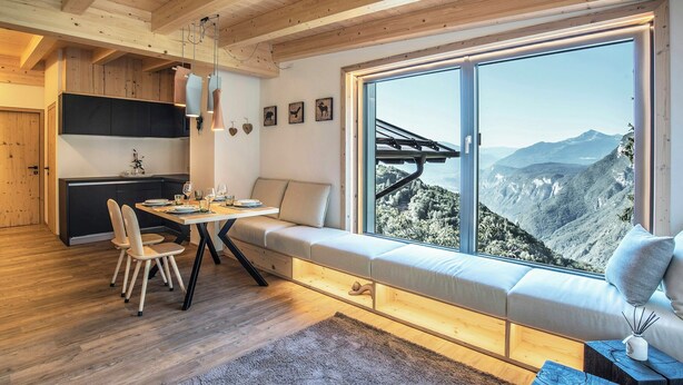 A modern interior with a dining area, a built-in bench with a view, and a large window overlooking a mountainous landscape. - Alpine flats in Fai della Paganella (Fai della Paganella)