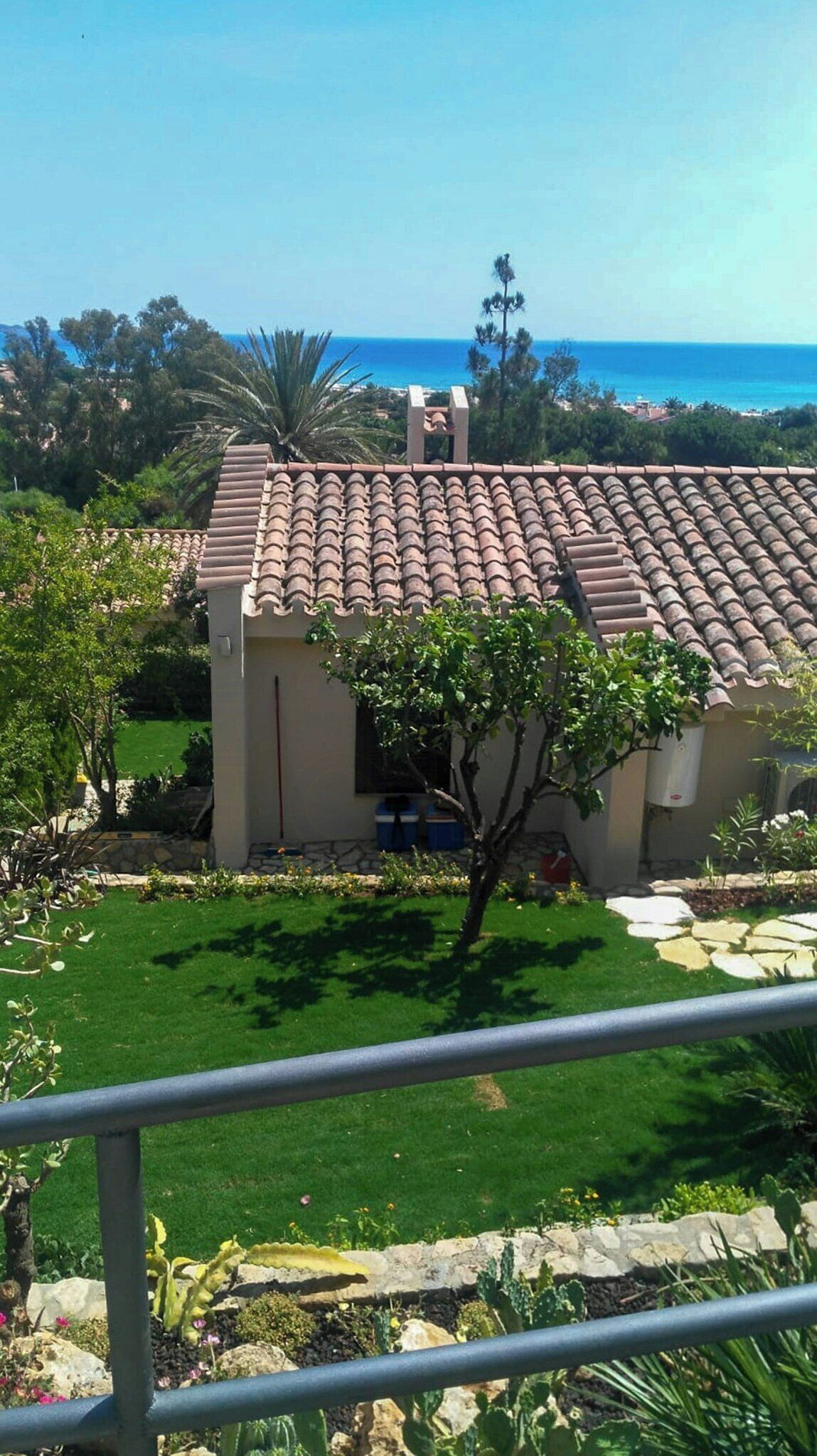 A house with a tiled roof, surrounded by greenery and a clear view of the ocean.
