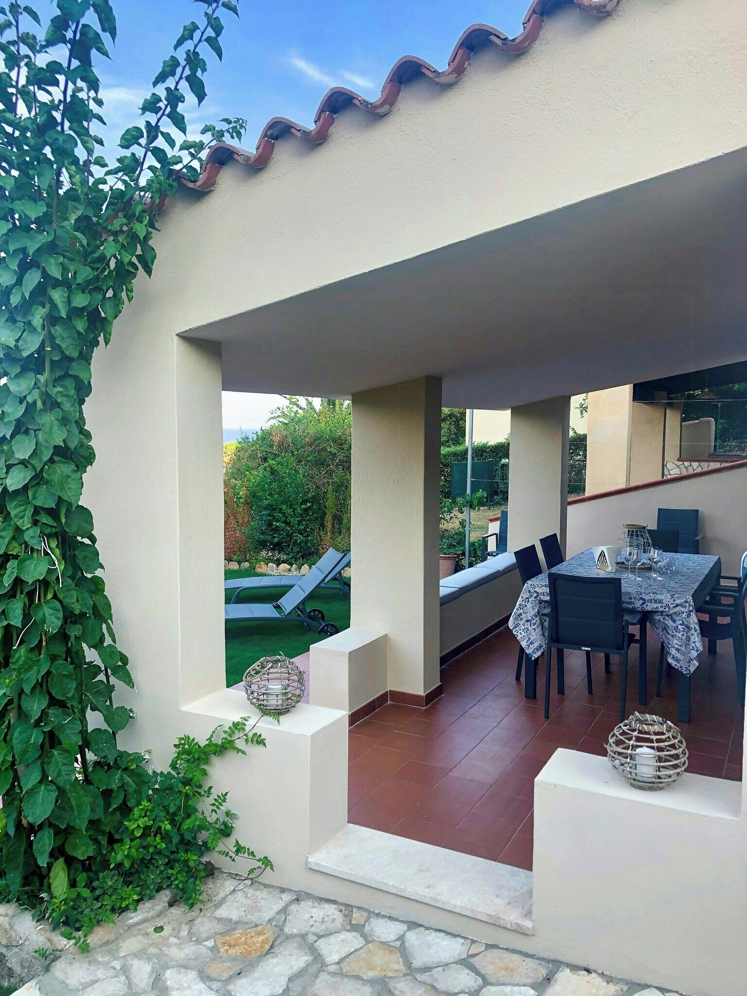 Un patio couvert avec une table et des chaises, un petit coin salon et une vue sur le jardin.