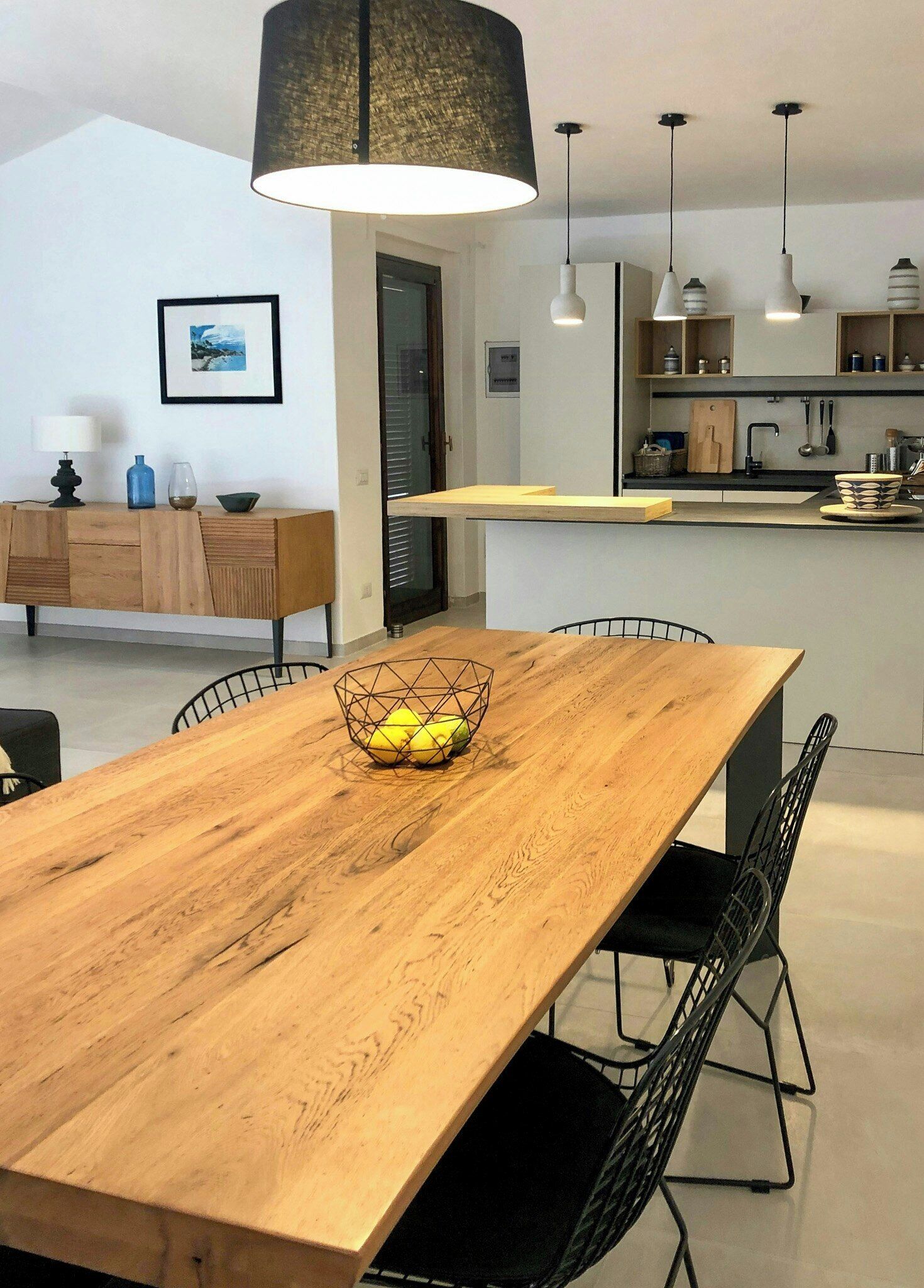 Une cuisine moderne avec une table à manger en bois, des chaises noires et des luminaires suspendus.