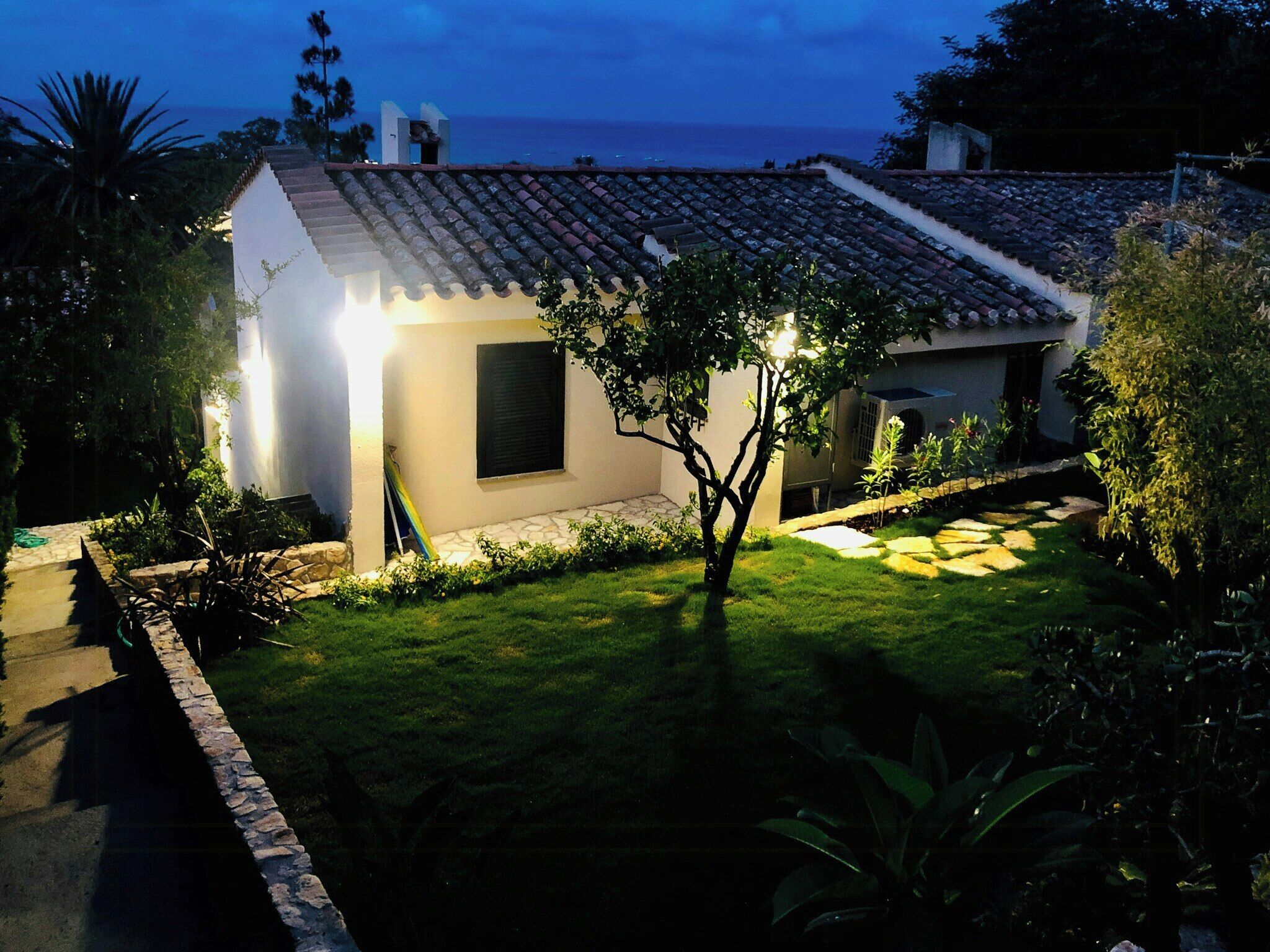 Una casa con tetto in tegole, un piccolo giardino e vista sul mare.