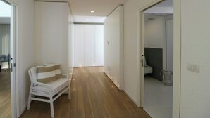 Een hal met een witte bank, houten vloeren en een badkamer zichtbaar door een geopende deur.
