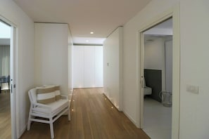 Ein Flur mit einem weißen Sofa, Holzböden und einem durchgehenden Türspalt sichtbaren Badezimmer.