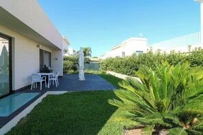 Ein modernes Gebäude mit Terrasse, Außenmöbeln und einem gepflegten Garten.