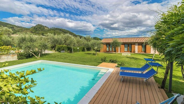 A swimming pool with lounge chairs, a wooden deck, and a house in the background. - Orlando. Villa with private pool near Lucca (Colle di Compito)
