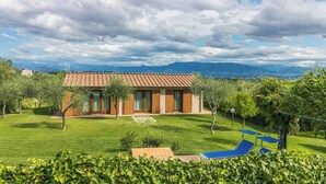 A modern house with a tiled roof, a well-maintained lawn, and a clear view of distant mountains. - Orlando. Villa with private pool near Lucca (Colle di Compito)