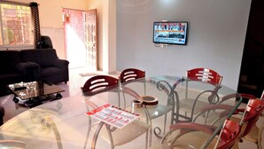 Una habitación con una mesa de vidrio rodeada de sillas, un sofá y un televisor en la pared.