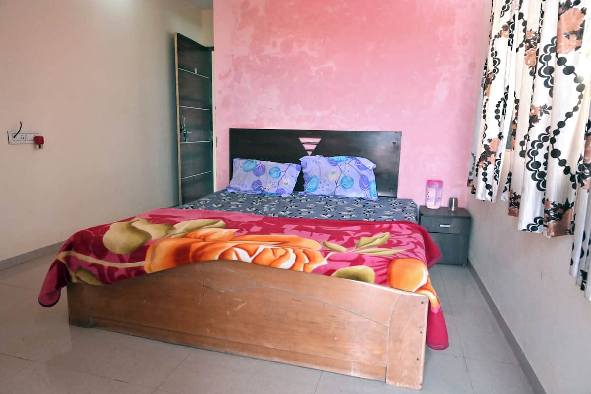 A bedroom with a wooden bed, a pink wall, and a patterned bedspread.