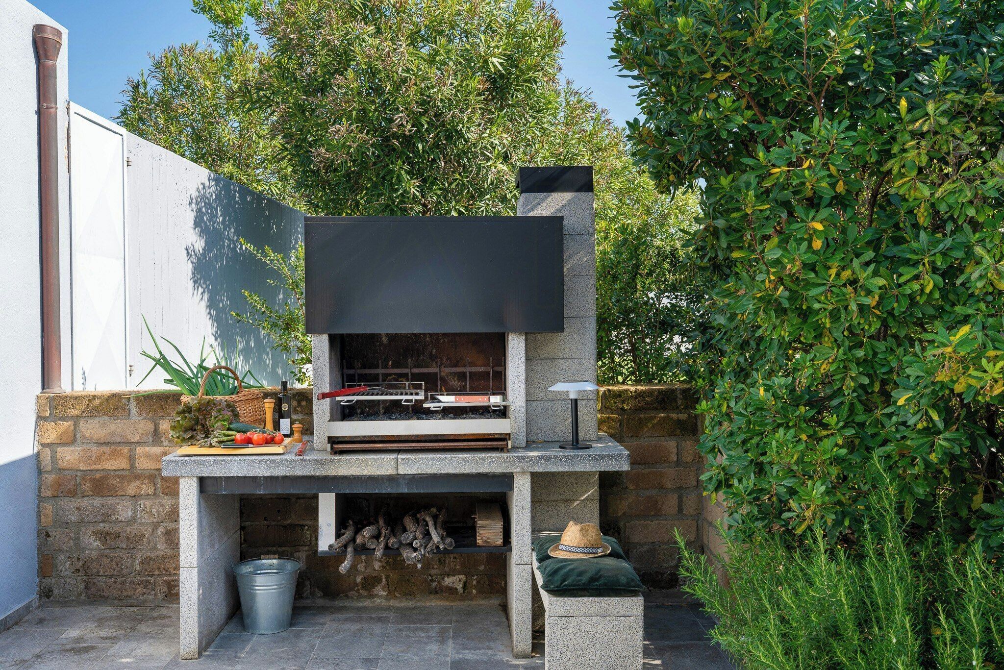 Une cuisine extérieure dotée d’un barbecue encastré, d’un mur en pierre et d’un seau en métal.