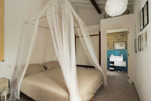 A bedroom with a canopy bed, a bathroom with a blue wall, and a hanging light fixture. - Exclusive villa with panoramic pool and gym (Campagnatico)