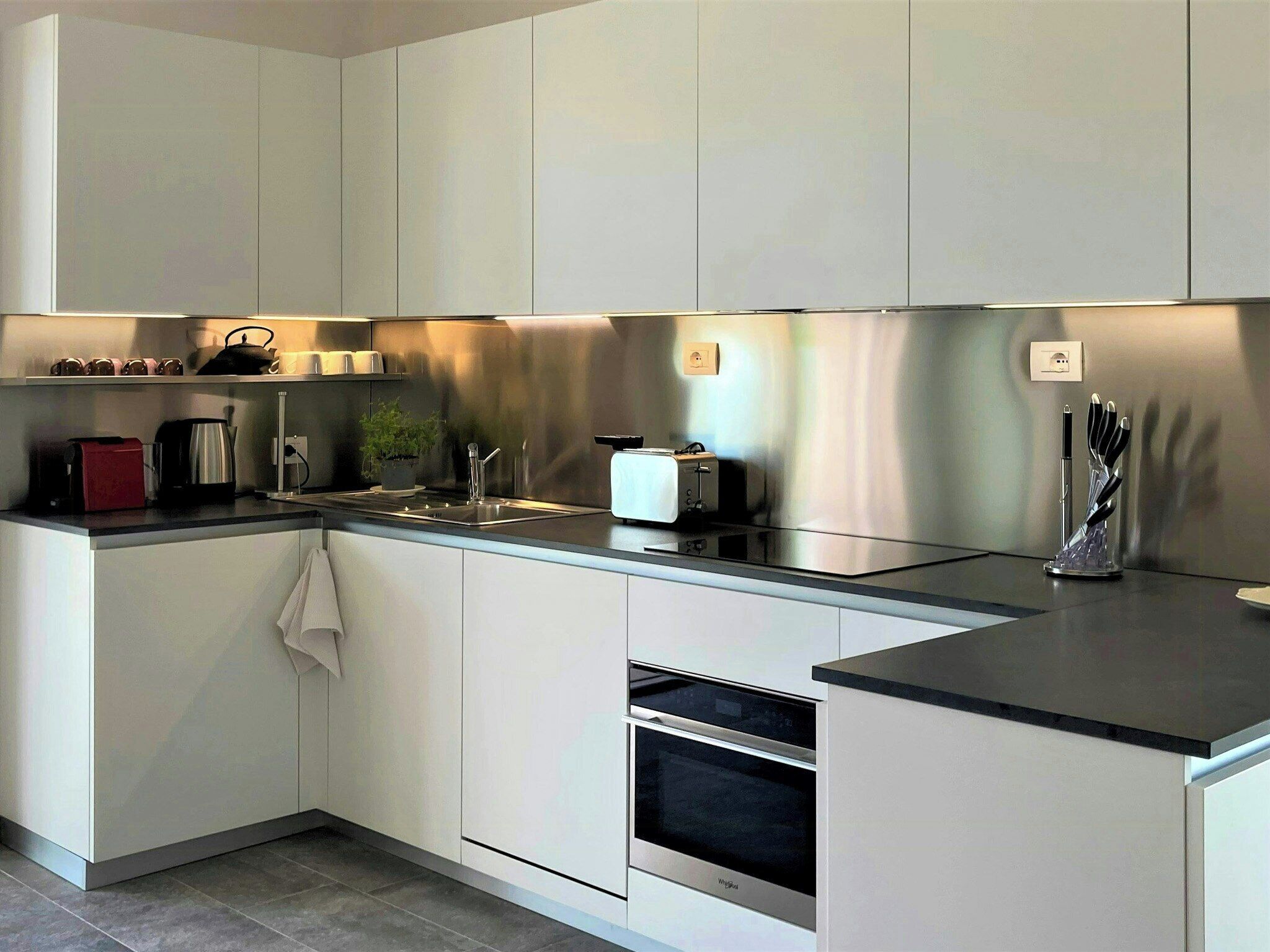 A modern kitchen with white cabinets, a stainless steel range hood, a toaster, a kettle, and a knife holder.