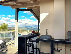 A balcony with a view of the sea and mountains, a bar area with stools, and a built-in sink. - Exclusive villa with panoramic pool and gym (Campagnatico)