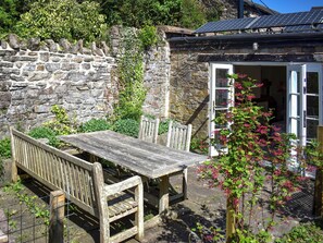 A stone wall, wooden bench, table, and a building with a door and solar panels. - 2 bedroom accommodation in Bampton (Bampton)
