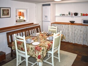 A dining area with a table set for four, chairs, a bench, a refrigerator, a shelf with kitchenware, and a window with a lamp. - 2 bedroom accommodation in Bampton (Bampton)