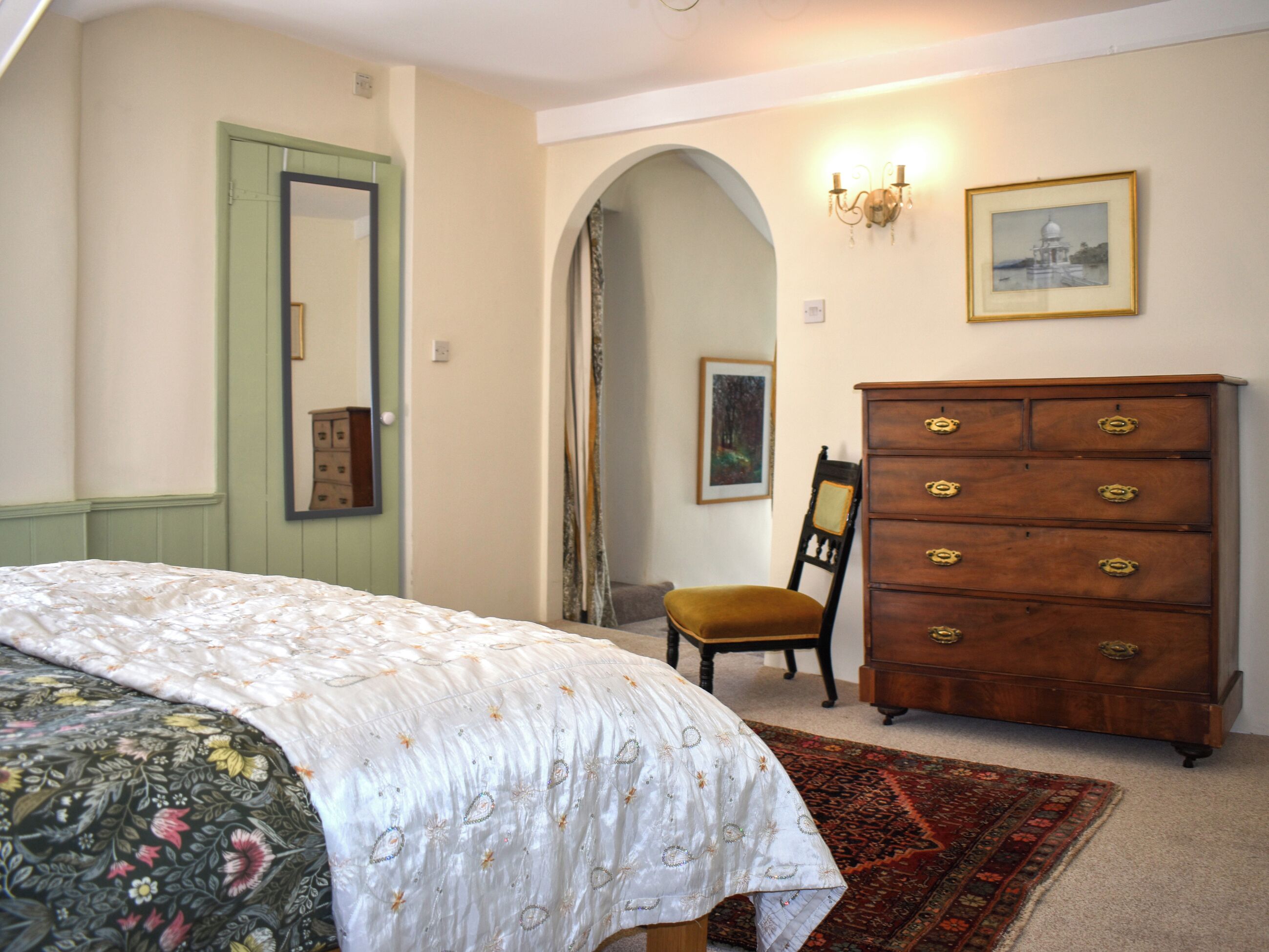 A bedroom with a bed, dresser, chair, and a mirror.