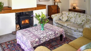 Ein Wohnzimmer mit Kamin, Blumensofa, einem gemusterten Tisch und einem Blumenstrauß.