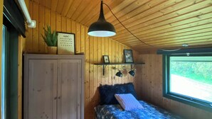 Une pièce de cabane en bois comprenant un lit, une armoire, une lampe suspendue et une fenêtre donnant sur un paysage agréable.