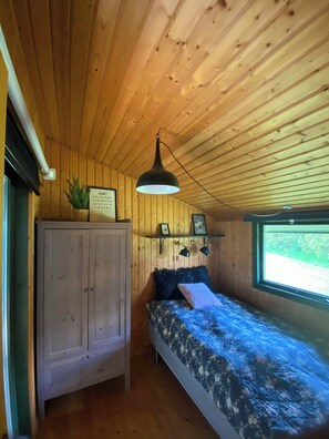 Ein Zimmer in einer Holzhütte mit einem Bett, einem Schrank, einer Hängeleuchte und einem Fenster mit Aussicht.