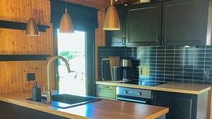 Une cuisine moderne dotée d’un îlot central, de meubles de rangement aux couleurs sombres et de luminaires suspendus.