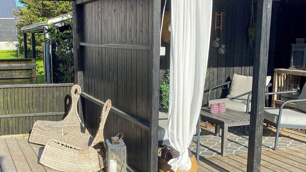 Une terrasse en bois avec une chaise en osier, une petite table et un rideau blanc.