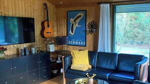 Un salon avec un canapé bleu, une table basse en verre, une guitare, un téléviseur et une affiche représentant un oiseau.
