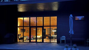 Ein modernes Gebäude mit großen Fenstern, einer Holzterrasse und Sitzgelegenheiten im Freien.