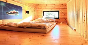 Ein Schlafzimmer einer Holzhütte mit einem Bett, einem Fenster und einer Wandleuchte.