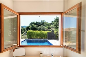 A room with a view of a swimming pool, a chair, and a table. - Historic Provençal farmhouse with pool in Provence (Le Plan-de-la-Tour)