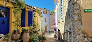 A narrow street with buildings, a blue door, and a sign pointing to the museum. - Historic Provençal farmhouse with pool in Provence (Le Plan-de-la-Tour)