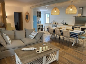 Ein modernes Wohnzimmer mit einer Couch, einem Esstisch und Stühlen, verbunden mit einer Küchenzeile inklusive Herd und Schränken.