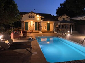 Ein Poolbereich mit Liegestühlen, einem Pool und einem Gebäude mit steinverkleideter Fassade und grünen Türen.
