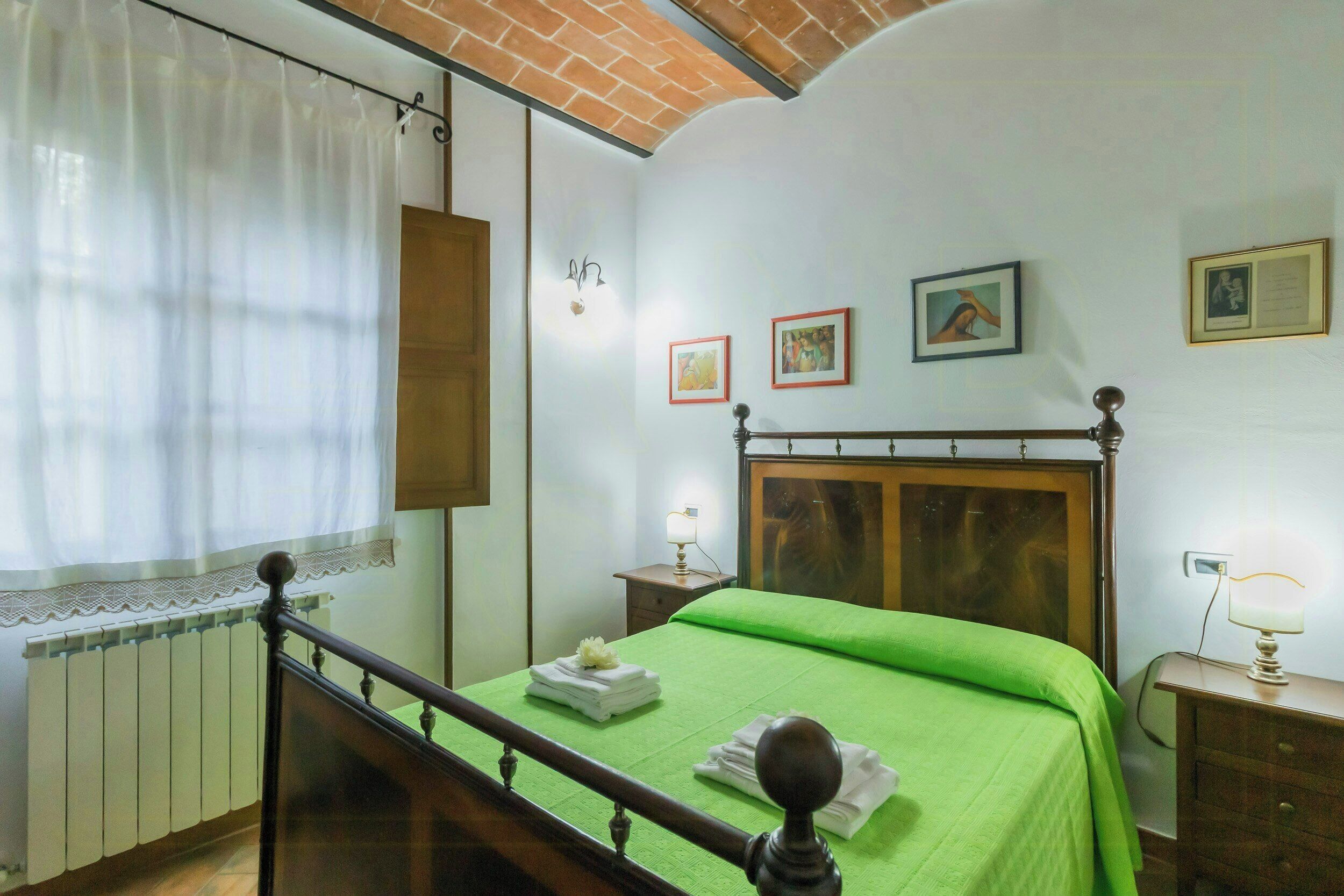 Una camera da letto con un letto di legno, un termosifone, un comodino con una lampada e opere d'arte alle pareti.